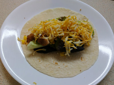 Taco with salad greens, chicken nuggets, and cheese